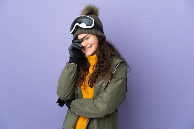 Teenager russian woman with snowboarding glasses isolated on\
purple wall laughing