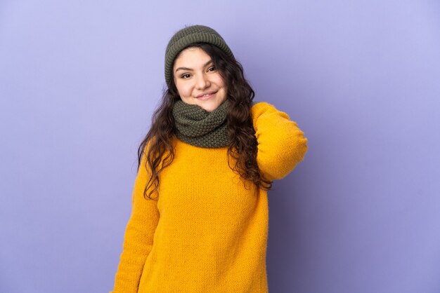 Русская женщина-подросток в зимней шапке изолирована на фиолетовой стене, смеясь