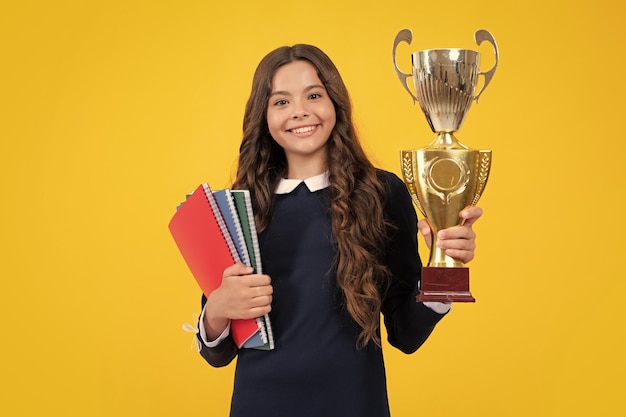 Teenager school girl with award winner trophy Child hold books with gold trophy or winning cup isolated on yellow Education graduation victory and winning