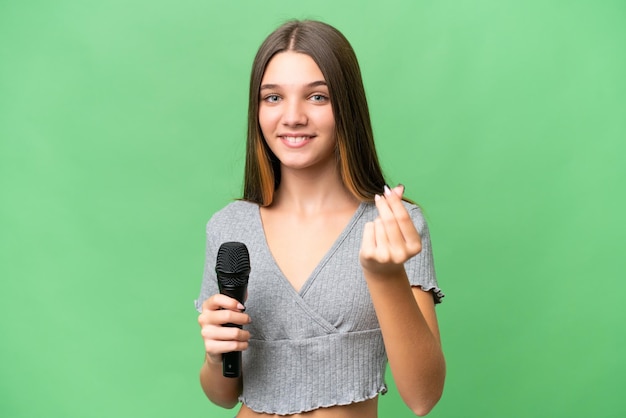 Teenager singer girl picking up a microphone over isolated background making money gesture