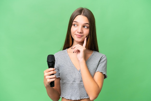 Teenager singer girl picking up a microphone over isolated background thinking an idea while looking up