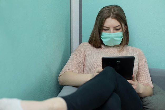 The teenager sits on a bed in a dormitory in a protective mask