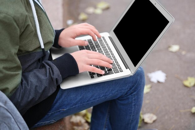 Teenager sitting on parapet with laptop in autumn day close up