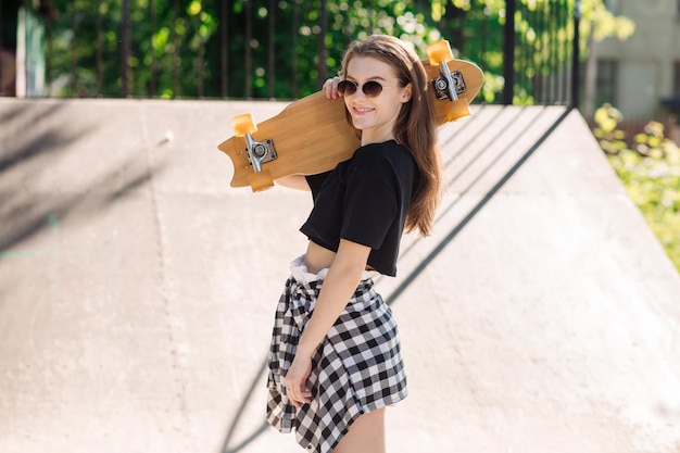 Teenager skater girl holding skateboard and standing in the skaters park