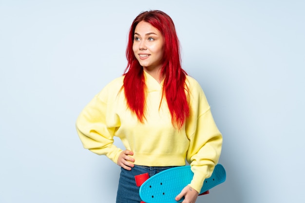 Teenager skater woman isolated on white wall posing with arms at hip and smiling