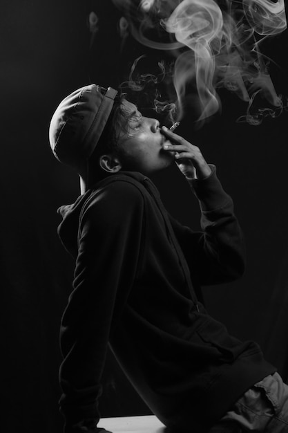 a teenager in a smoking hat on a black background and smoking in a photo studio room