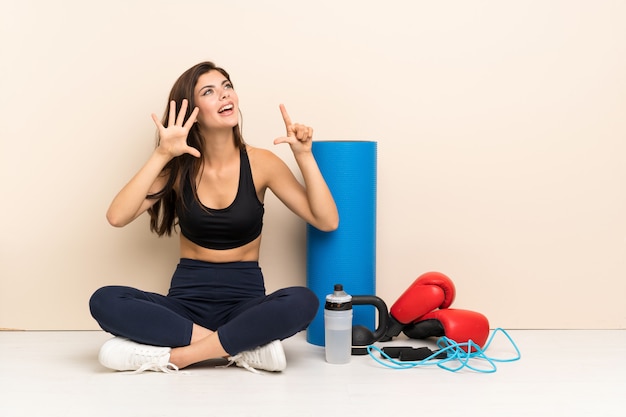 Ragazza di sport dell'adolescente che si siede sul pavimento che conta sette con le dita