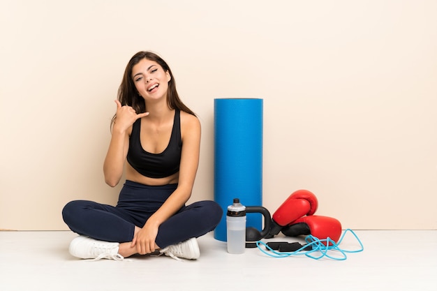 Teenager sport girl sitting on the floor making phone gesture. Call me back sign