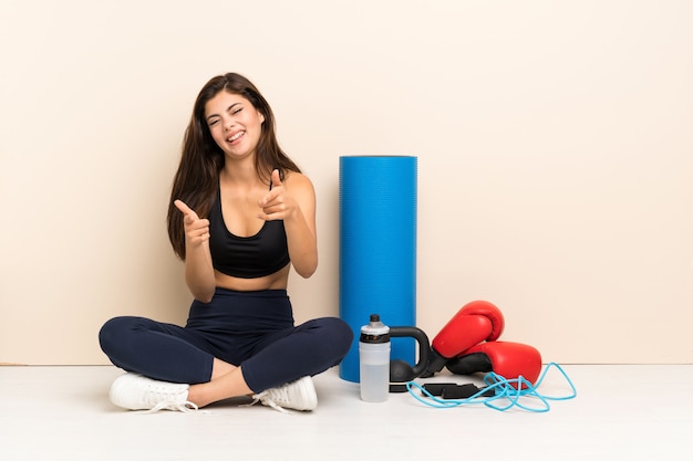 Teenager sport girl sitting on the floor pointing to the front and smiling