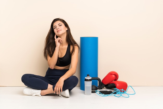 Teenager sport girl sitting on the floor thinking an idea while looking up