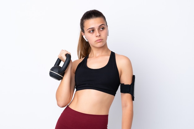 Teenager sport woman over isolated white wall making weightlifting with kettlebell