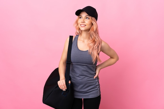 Teenager sport woman with sport bag over isolated wall thinking an idea while looking up