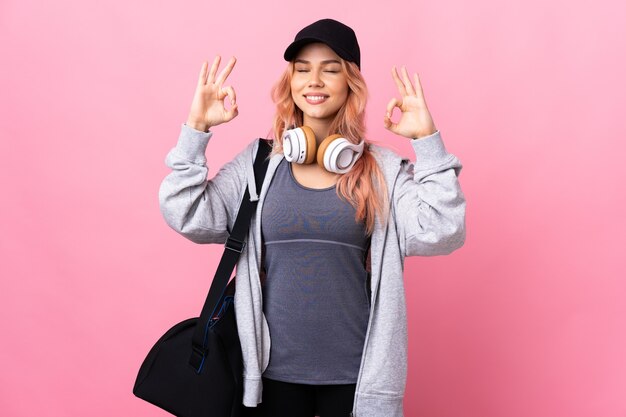 Teenager sport woman with sport bag over isolated wall in zen pose