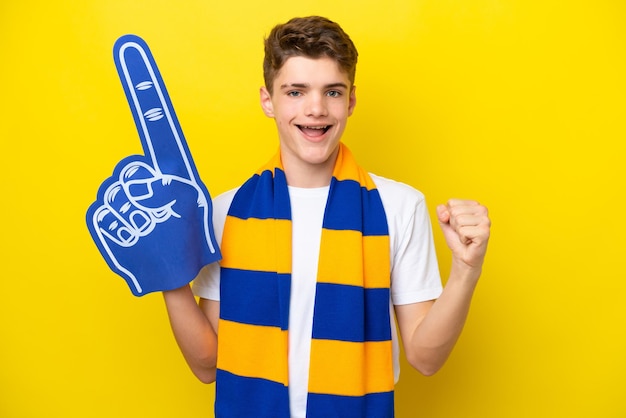 우승자 위치에서 승리를 축하하는 노란색 배경에 고립 된 십대 스포츠 팬 남자