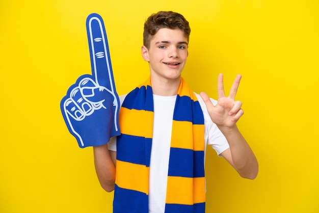 Teenager sports fan man isolated on yellow background happy and counting three with fingers