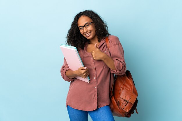 親指を立てるジェスチャーを与える青に分離された10代の学生の女の子