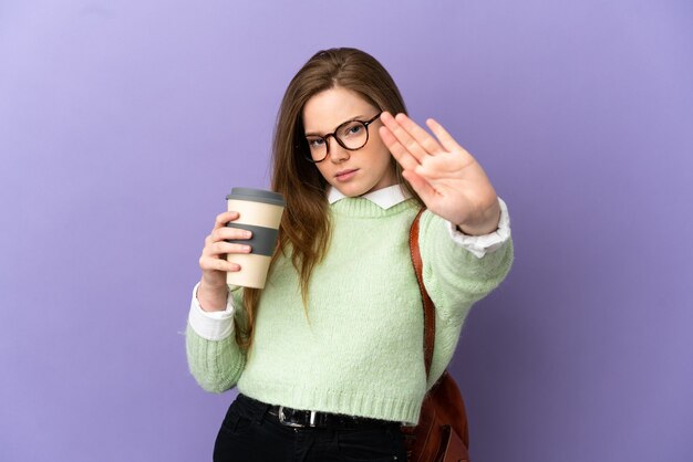 Teenager student girl over isolated purple background making stop gesture and disappointed