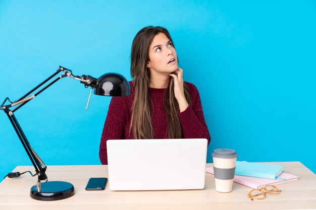 Teenager student girl in a workplace over blue wall