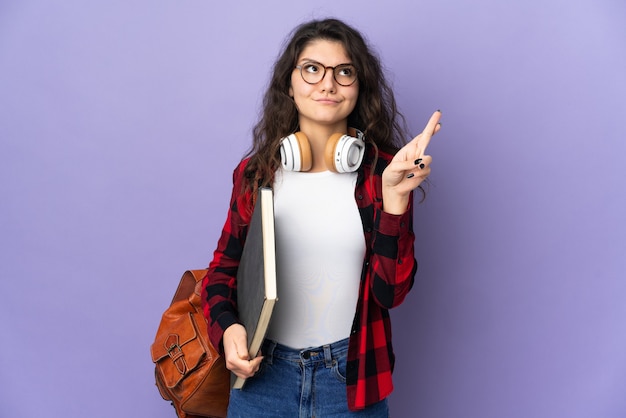 Teenager student isolated on purple background with fingers crossing and wishing the best