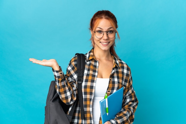 Teenager student Russian girl isolated on blue wall holding copyspace imaginary on the palm to insert an ad