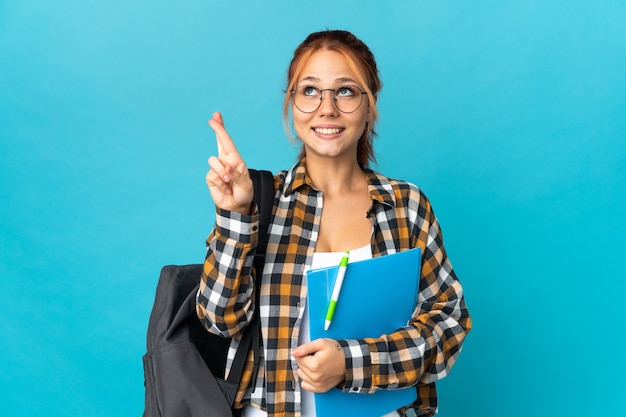 Teenager student Russian girl isolated on blue wall with fingers crossing and wishing the best