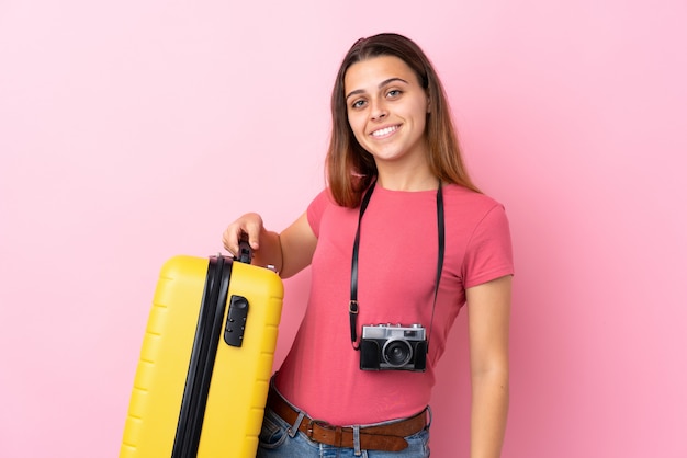 Teenager traveler girl holding a suitcase over isolated pink smiling a lot