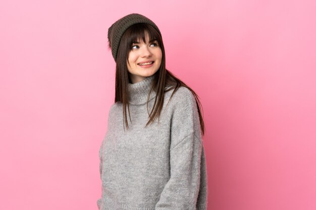 Teenager Ukrainian girl with winter hat isolated on white background laughing and looking up