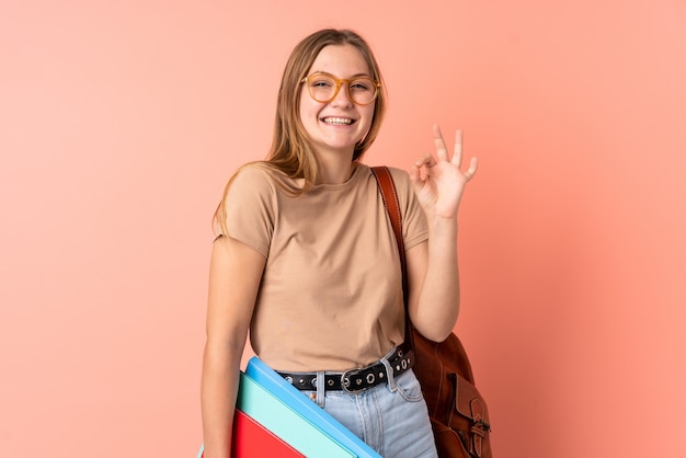 Teenager Ukrainian student woman isolated on pink space showing an ok sign with fingers