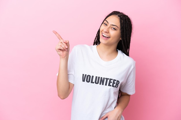 Teenager volunteer girl with braids isolated on pink background pointing finger to the side and presenting a product