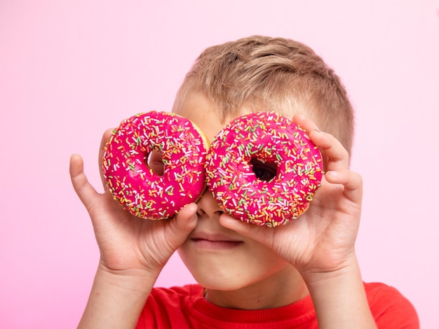 The teenager was having fun with donuts looking through them. a boy is having fun with donuts on a pink background. fun time with food