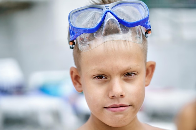 Teenager wearing blue goggles on forehead demonstrates funny\
grimaces on blurry beach