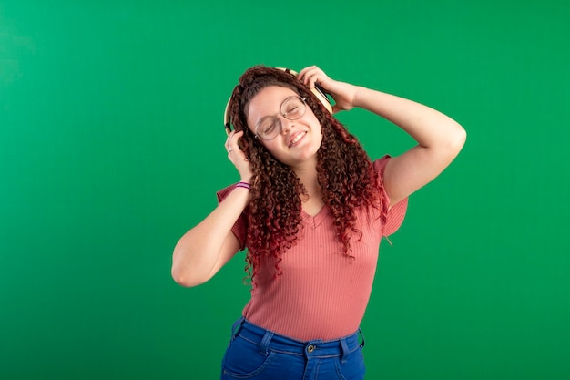 Teenager wearing glasses wearing a headset in fun poses in a studio shot with a green background ideal for cropping