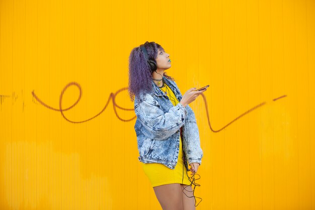 Teenager with afro hair listening to music on a yellow wall