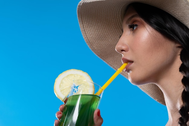 A teenager with an alcoholic drink in her hand and a large hat basks in the summer sun