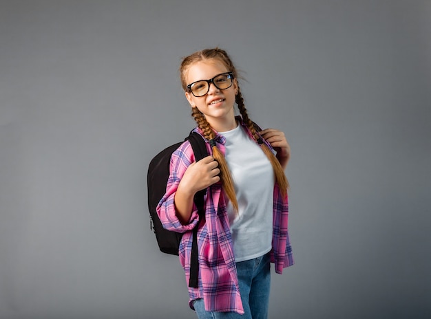 Teenager with a backpack. Cute smiling schoolgirl. Little schoolgirl girl carries a backpack. A student with long braids goes to school.