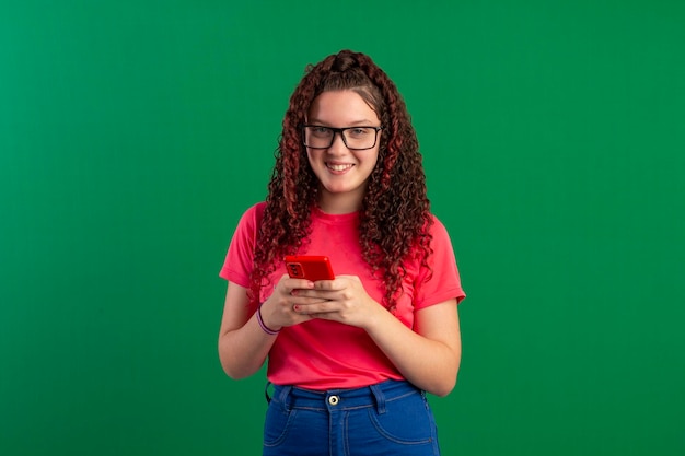 Teenager with glasses using cell phone in fun poses in studio photo with green background ideal for cropping