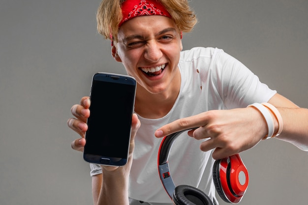 Teenager with headphones and phone, young man in a light t-shirt against a gray wall background