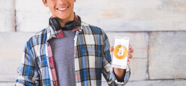 Teenager with headphones standing and show bitcoin in his phone - he is smile - future money and payment metod - new generations