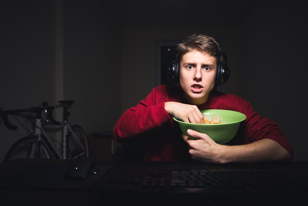 Photo teenager with a serious face sits in the headphones at night at the computer