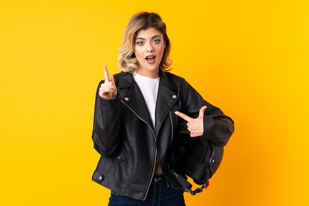 Teenager woman holding a motorcycle helmet isolated on yellow with surprise facial expression