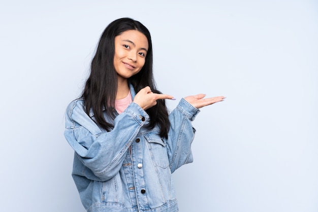 Teenager woman isolated on blue holding copyspace imaginary on the palm to insert an ad