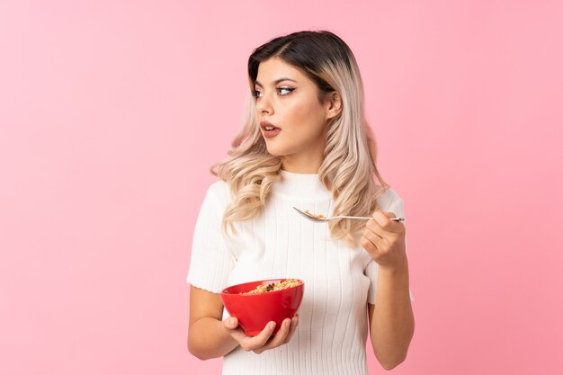 Teenager woman over isolated pink holding a bowl of cereals and thinking