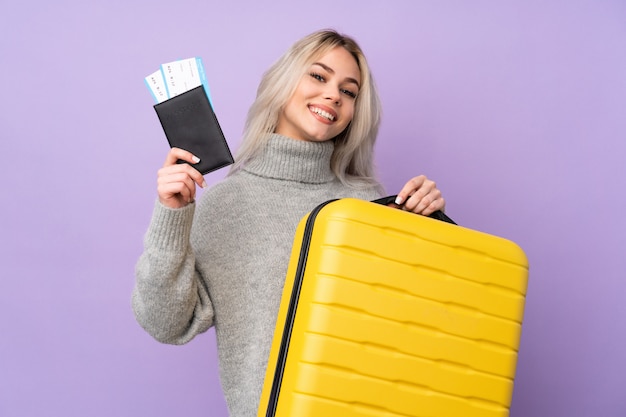 Teenager woman over isolated purple wall in vacation with suitcase and passport