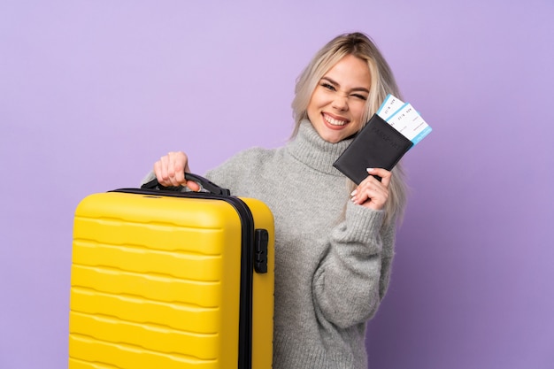 Teenager woman over isolated purple wall in vacation with suitcase and passport