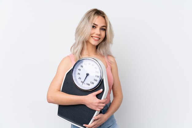 Teenager woman over isolated white wall with weighing machine