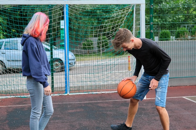10대 소년과 소녀가 함께 거리 농구를 하고, 유행하는 헤어스타일을 한 젊은이들이 야외에서 놀고 있습니다. 활동적인 건강한 생활 방식, 취미 및 여가, 십대 개념