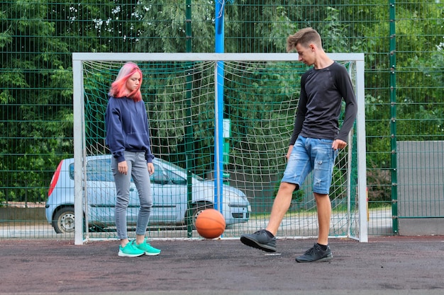 Teenagers boy and girl playing street basketball together, youth with trendy hairstyles playing outdoors. Active healthy lifestyle, hobbies and leisure, teenagers concept