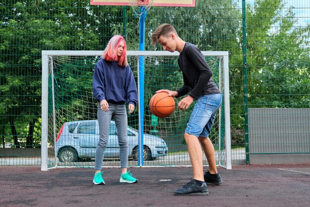 Teenagers boy and girl playing street basketball together, youth with trendy hairstyles playing outdoors. Active healthy lifestyle, hobbies and leisure, teenagers concept