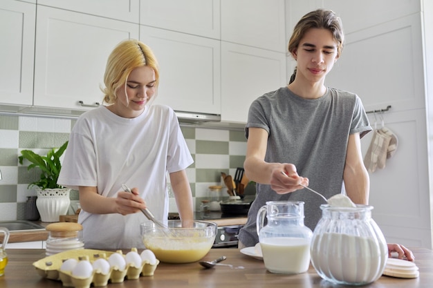 Teenagers guy and girl cooking pancakes in kitchen together