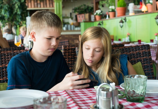 카페에서 휴대폰으로 즐거운 시간을 보내는 10대들 현대적인 생활 방식과 기술 개념 식당에 앉아 스마트폰을 보는 아이들